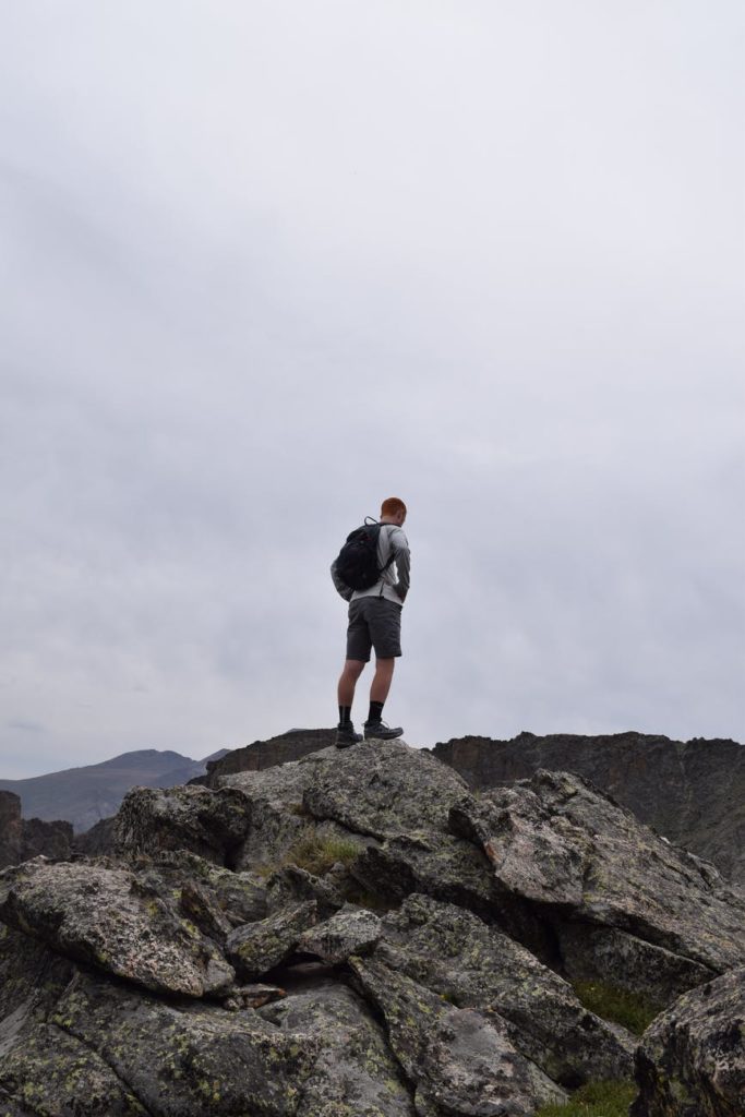 man with black backpack standing on rock