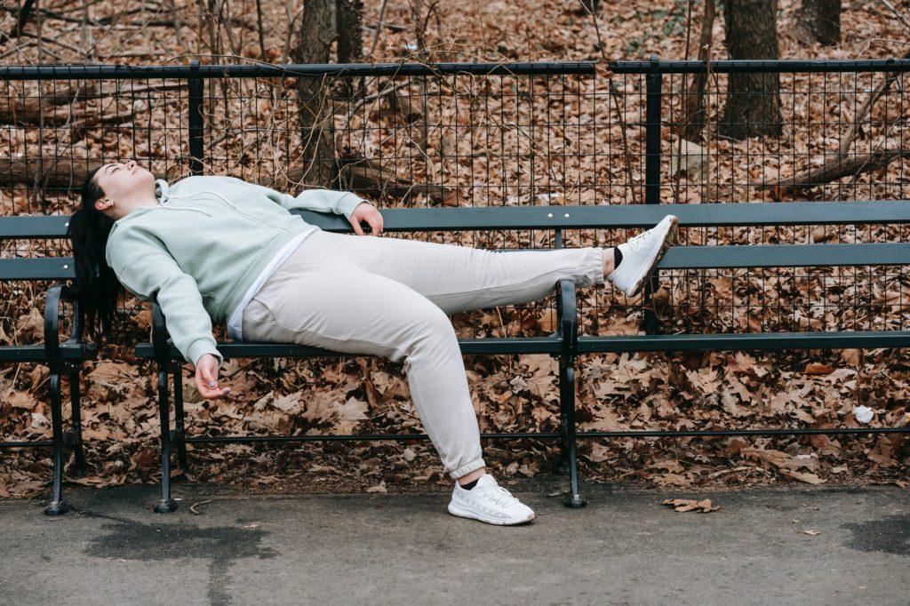 tired woman lying on bench in park